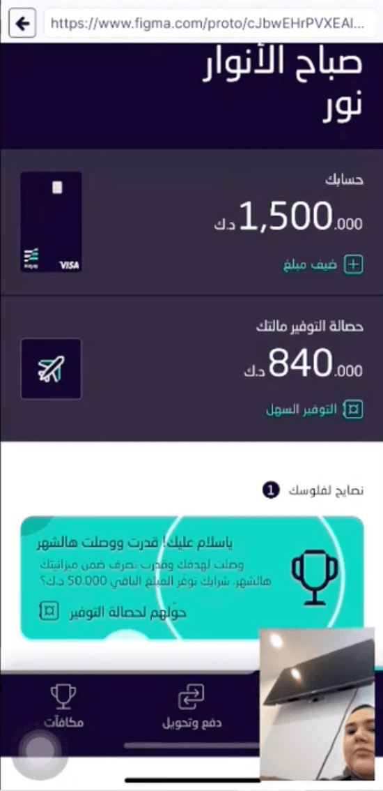 The Arabic prototype during a session, in the phone's browser: Home with a green card saying the month closed under budget, with a trophy. A small camera view in the corner shows the participant.